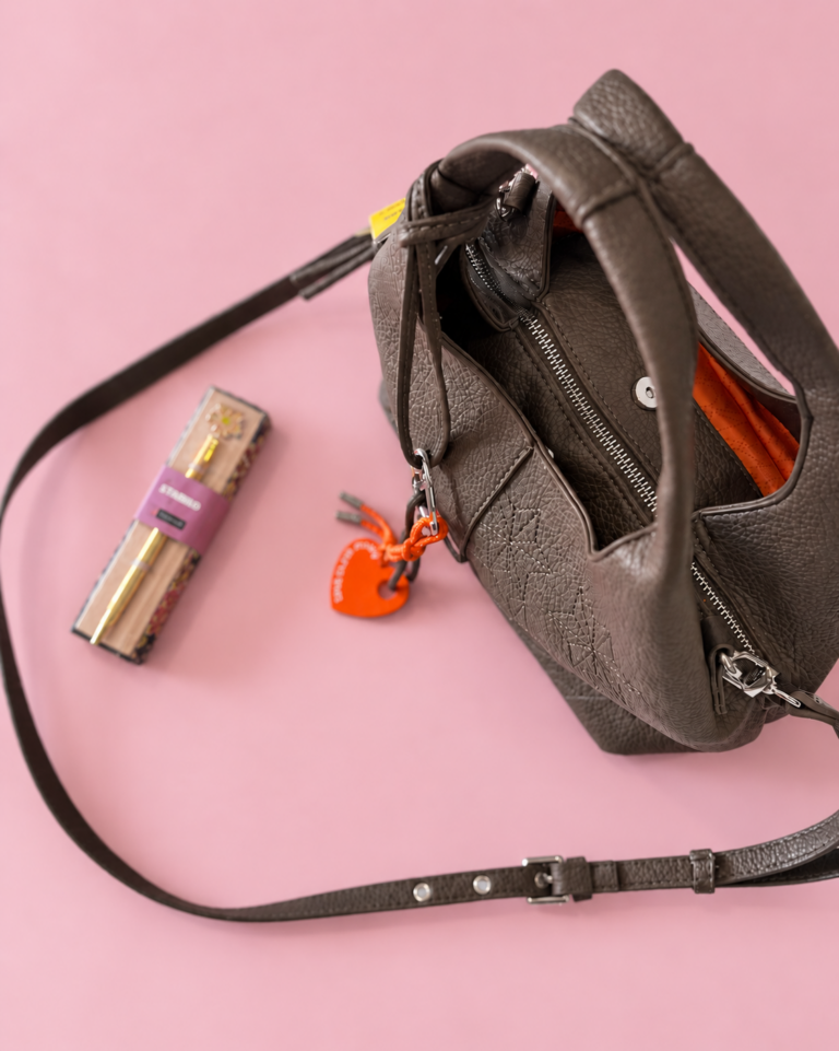 Bolso taupe y charm naranja sobre rosa